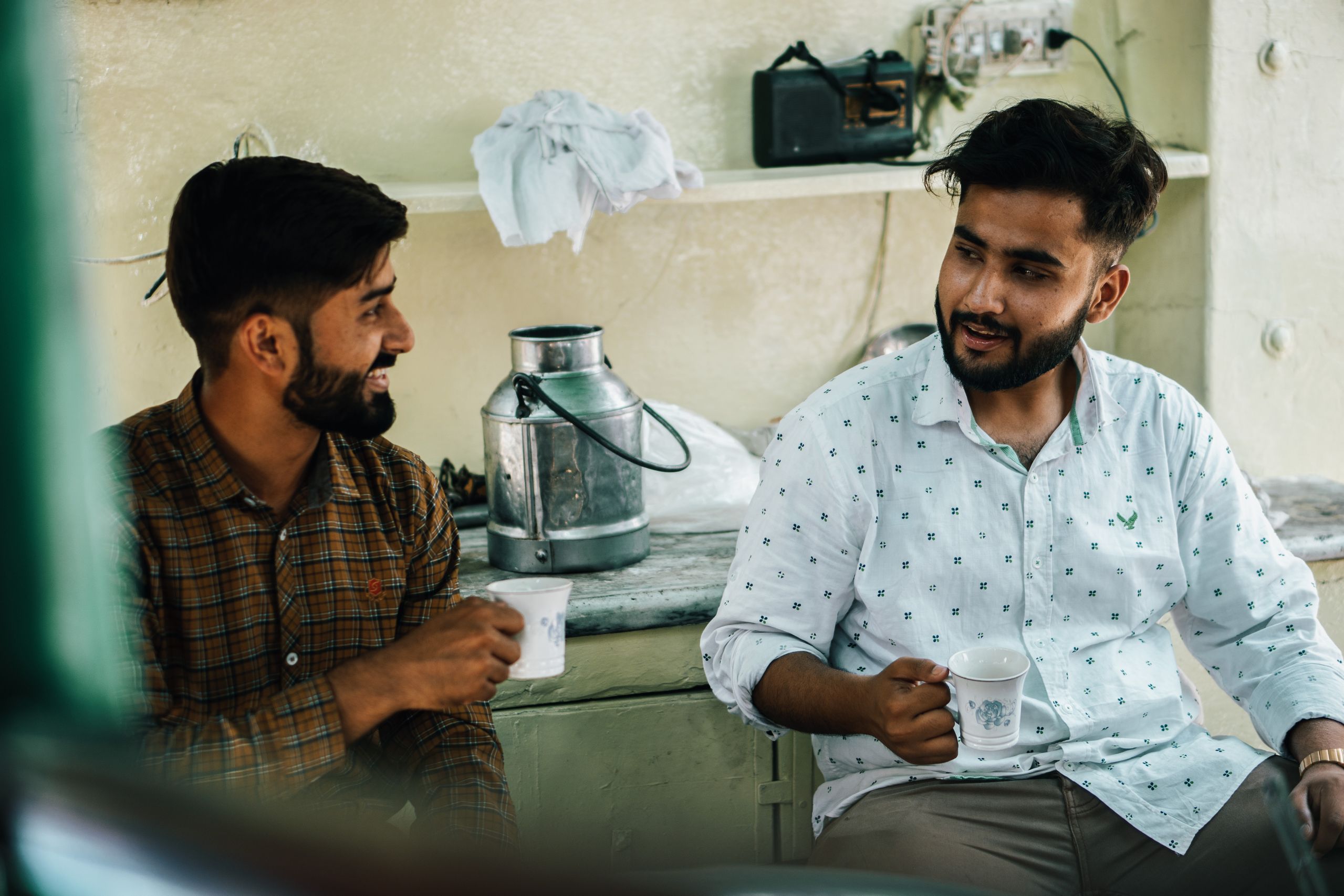 Two men in aprons talking and holding mugs